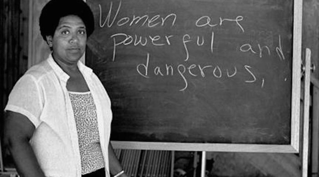 A black women in front of a chalk board that has the words "Women are powerful and dangerous"