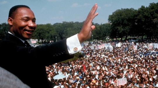 MLK jr. in front of a crowd waving during his "I have a Dream" speech.